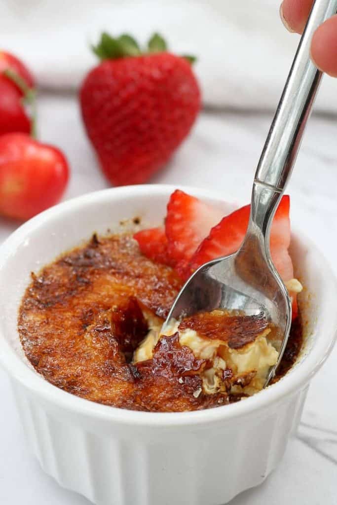 Cracking the Hardened Sugar on Breakfast Crème Brûlée in Small Ramekins with Strawberries on Top