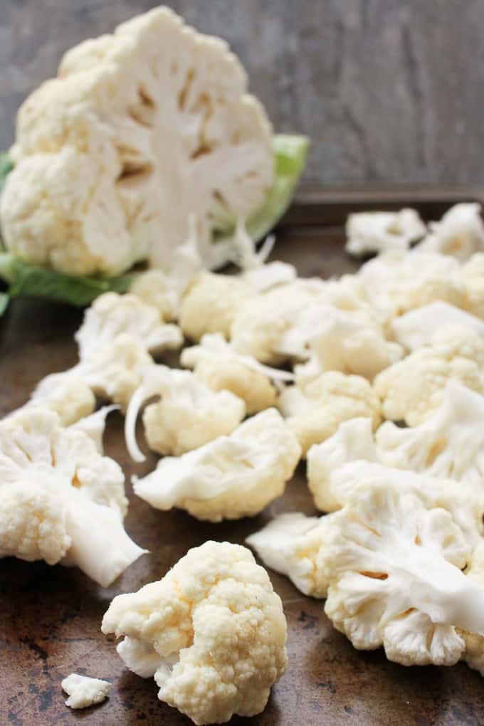 Cauliflower cut into bite-size pieces, with an uncut cauliflower in the background