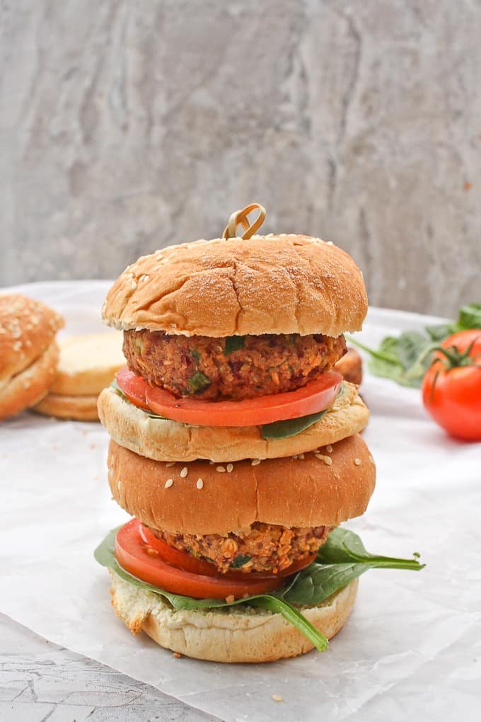 Vegan Quinoa Burgers stacked together with extra buns, lettuce, and tomato in the background