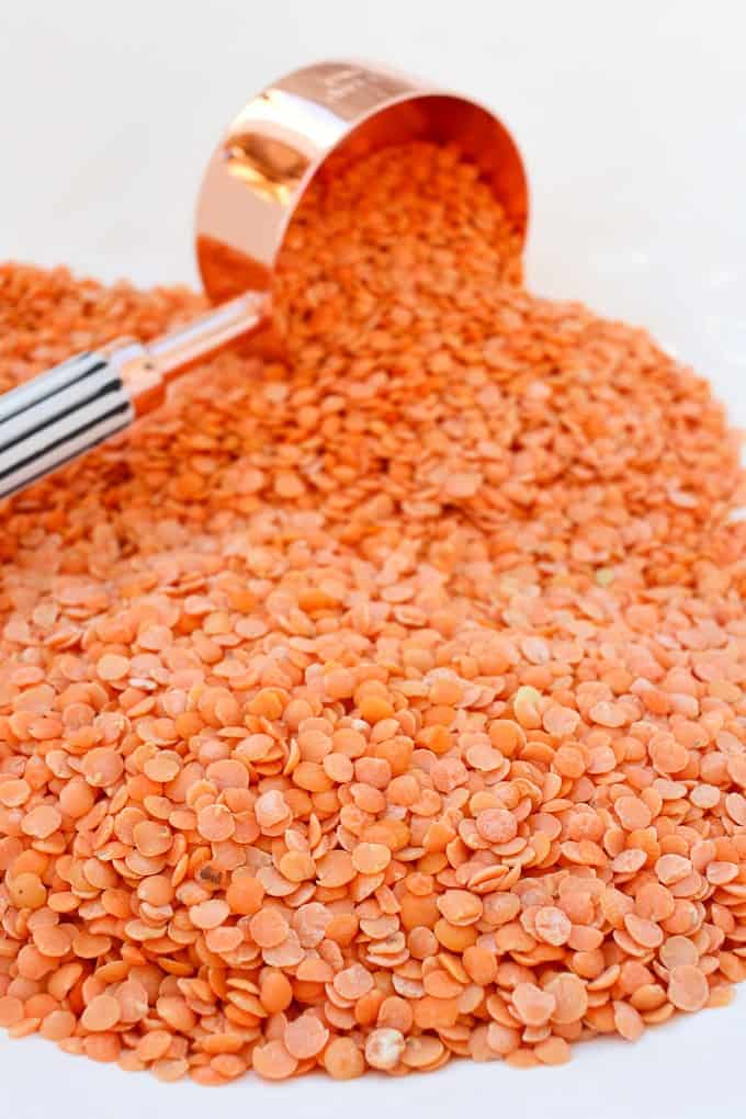 Red Lentils spilled on a counter, with a measuring cup resting in them
