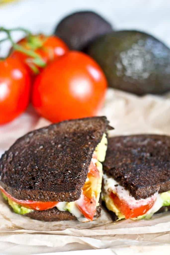 Washed rind cheese, tomato, avocado grilled in pumpernickel bread, with tomatoes and avocado in the background