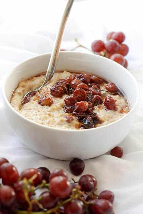 Roasted Grape Oatmeal in a bowl surrounded by red grapes. (The Best Oatmeal Recipe!)