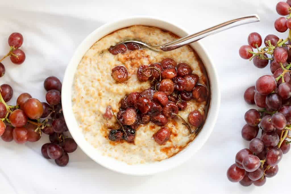 Roasted Grape Oatmeal in a bowl surrounded by red grapes.