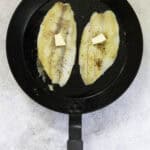 fish fillets topped with butter in hot pan.