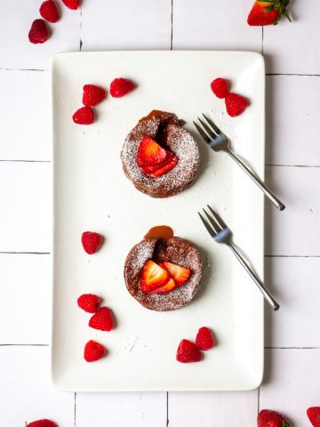 two chocolate lava cakes on a serving platter with berries