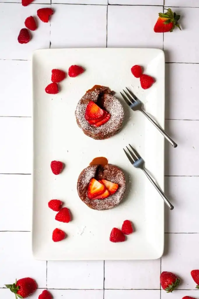 two chocolate lava cakes on a serving platter with berries