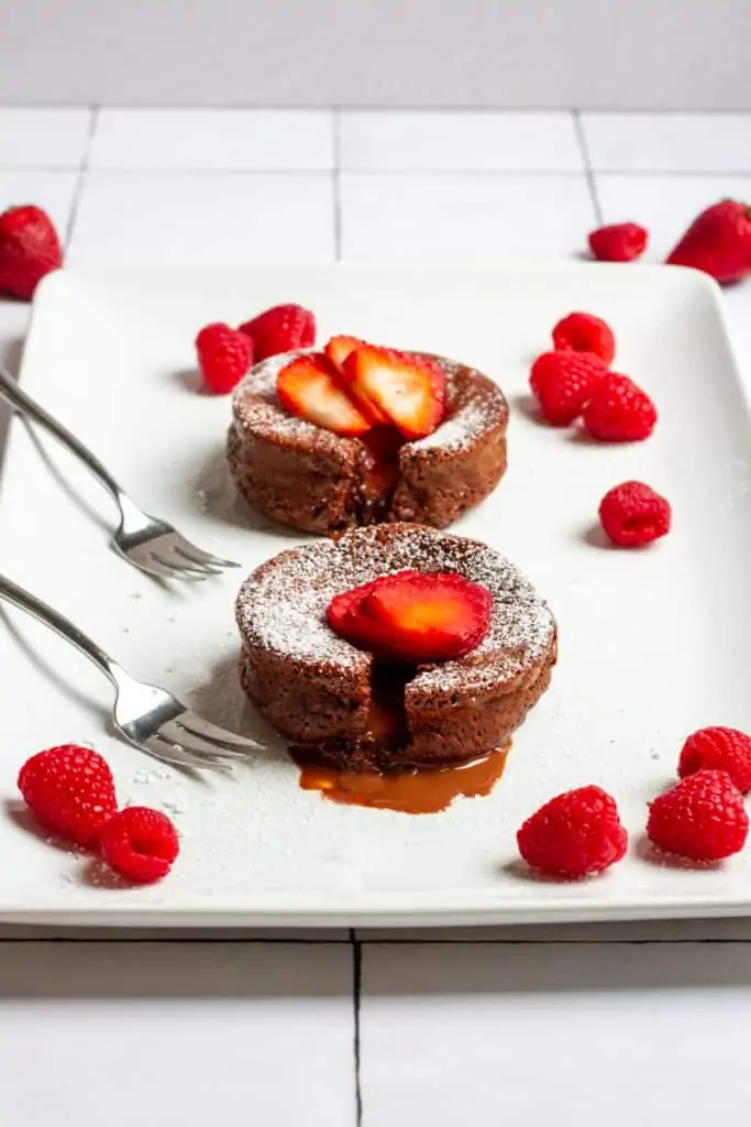 two chocolate lava cakes on a serving platter with berries