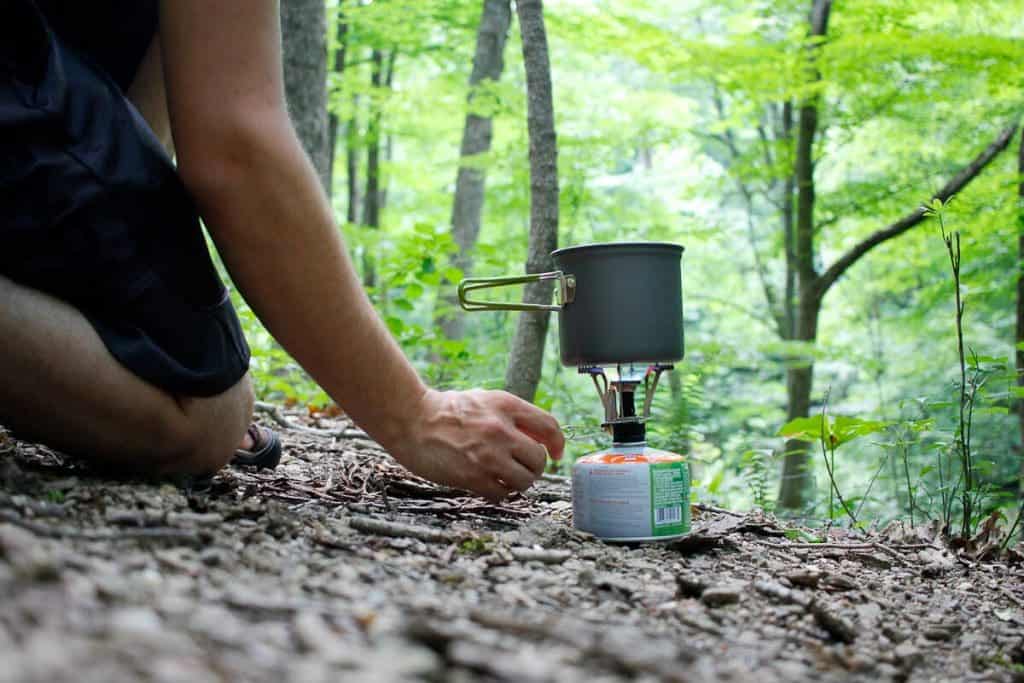 A person uses a backpacking stove to boil water in the woods.