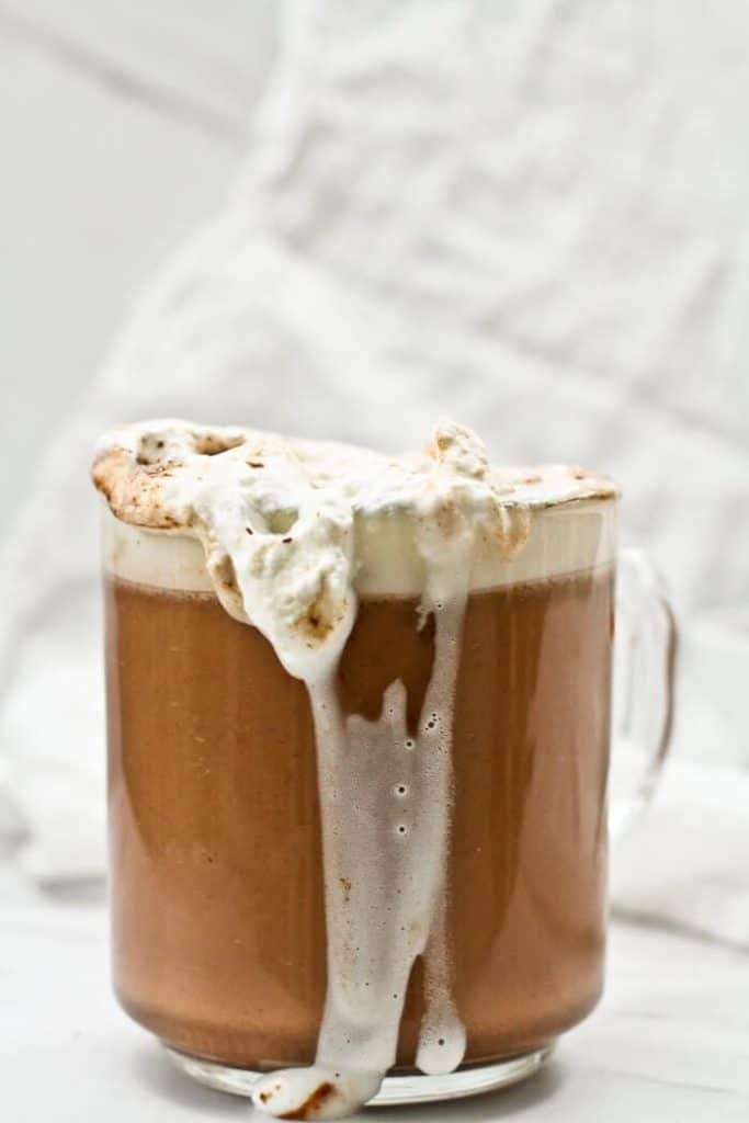 Pumpkin Spice Hot Chocolate in a see-through mug with whipped cream running over the edge of the mug.