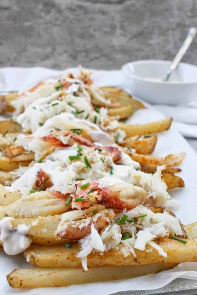 Baked fries on a serving platter, topped with melted smoked Gouda and fresh crab. Sauce is served on the side for dipping.