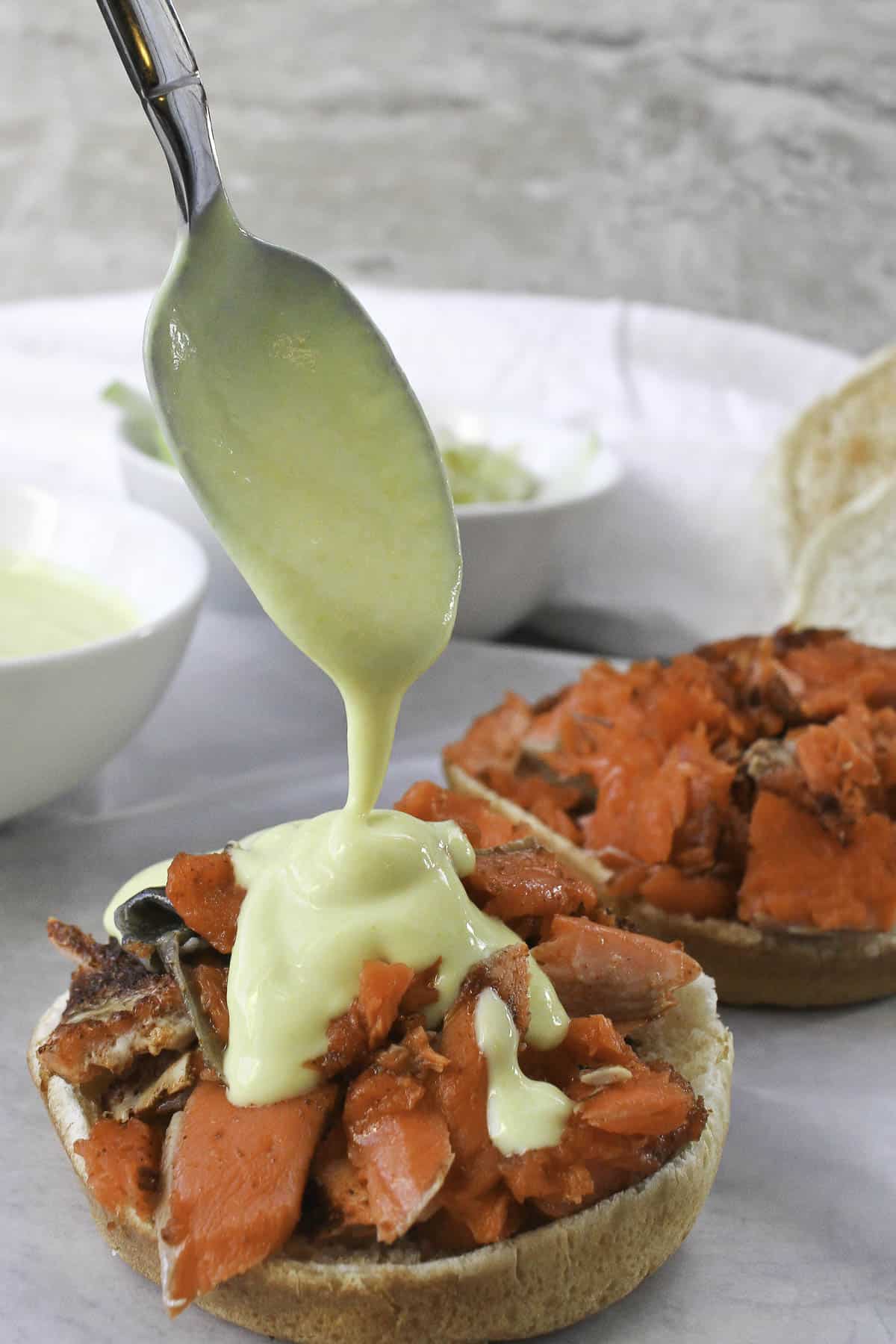 a spoon pouring mustard sauce on a salmon sandwich.