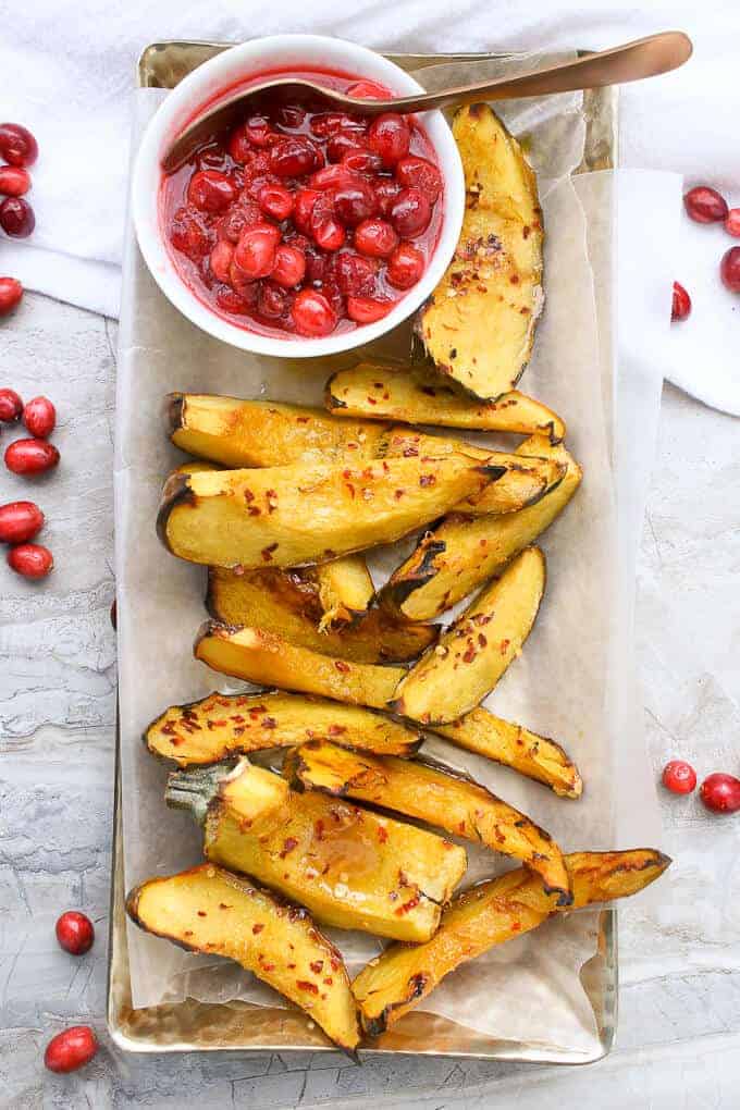 Maple Roasted Acorn Squash slices on a gold serving tray, with cranberry sauce on the side.
