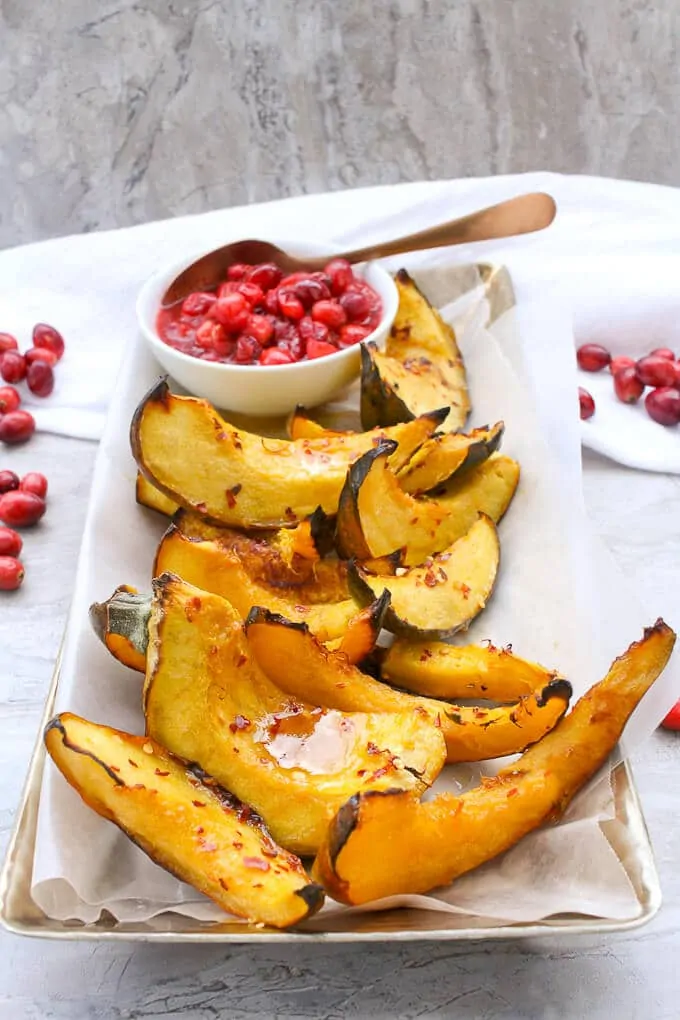 Cut and roasted acorn squash slices on a serving tray with cranberry sauce on the side.