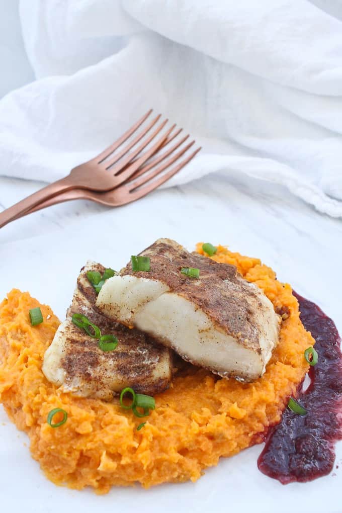 Two cod fillets stacked on top of sweet potato mash, with puréed raisin sauce on the side.