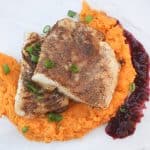 Two cod fillets stacked on top of sweet potato mash, with puréed raisin sauce on the side.