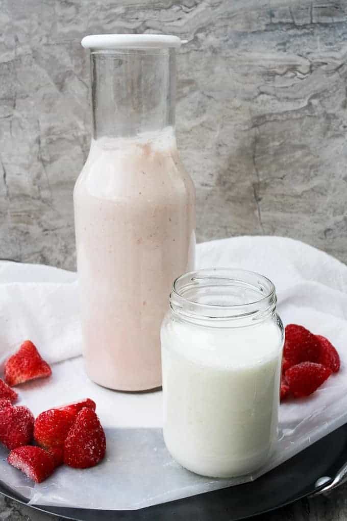 Plain kefir, strawberry kefir, and strawberries on a counter (how to make kefir milk).