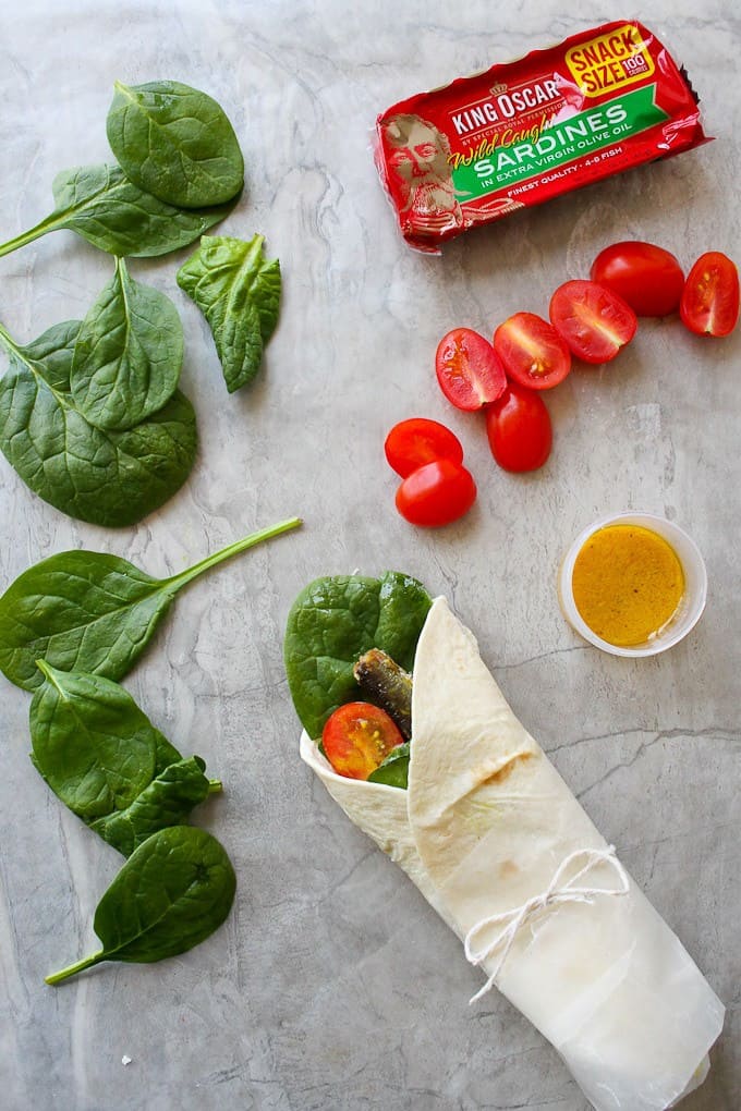 Fish wraps with sardines, tomatoes, dressing, and spinach on a countertop
