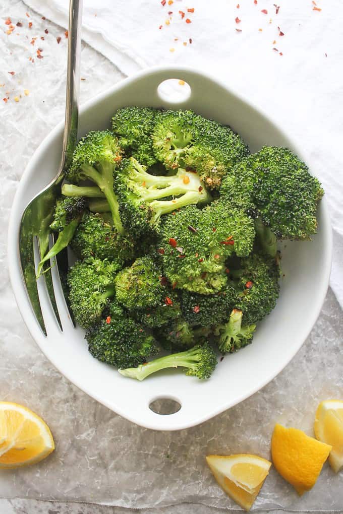 oven-roasted broccoli in a serving bowl, with lemon and chili flakes on the side