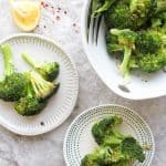 oven roasted broccoli in a serving bowl and on plates, with lemon and chili flakes on the side
