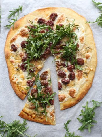 Arugula pizza with one slice cut out and extra arugula