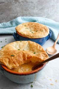 Seafood pot pie in bowls, with a spoon breaking through the puff pastry