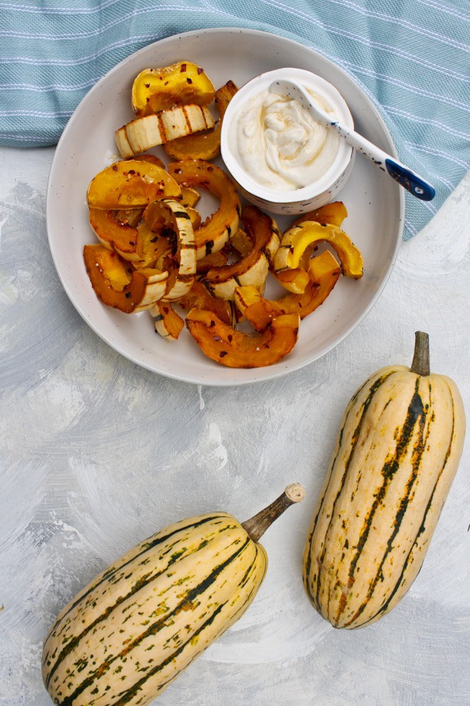 roasted delicata squash in a serving bowl with tahini yogurt sauce on the side.