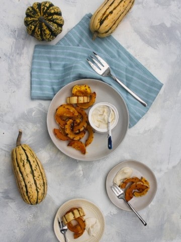 roasted delicata squash in a serving bowl with tahini yogurt sauce on the side