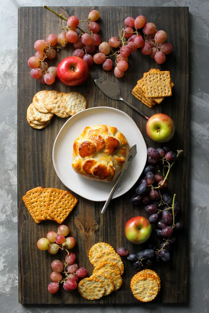 Baked brie in puff pastry on a cheese board with fruit and crackers.