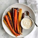 whole roasted carrots on a serving tray with tahini sauce