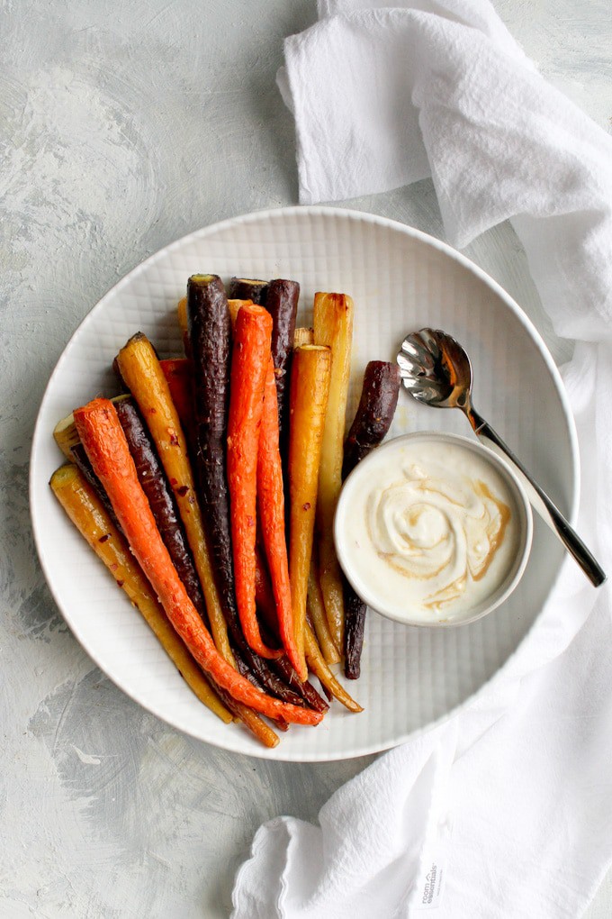 whole roasted carrots on a serving tray with tahini sauce