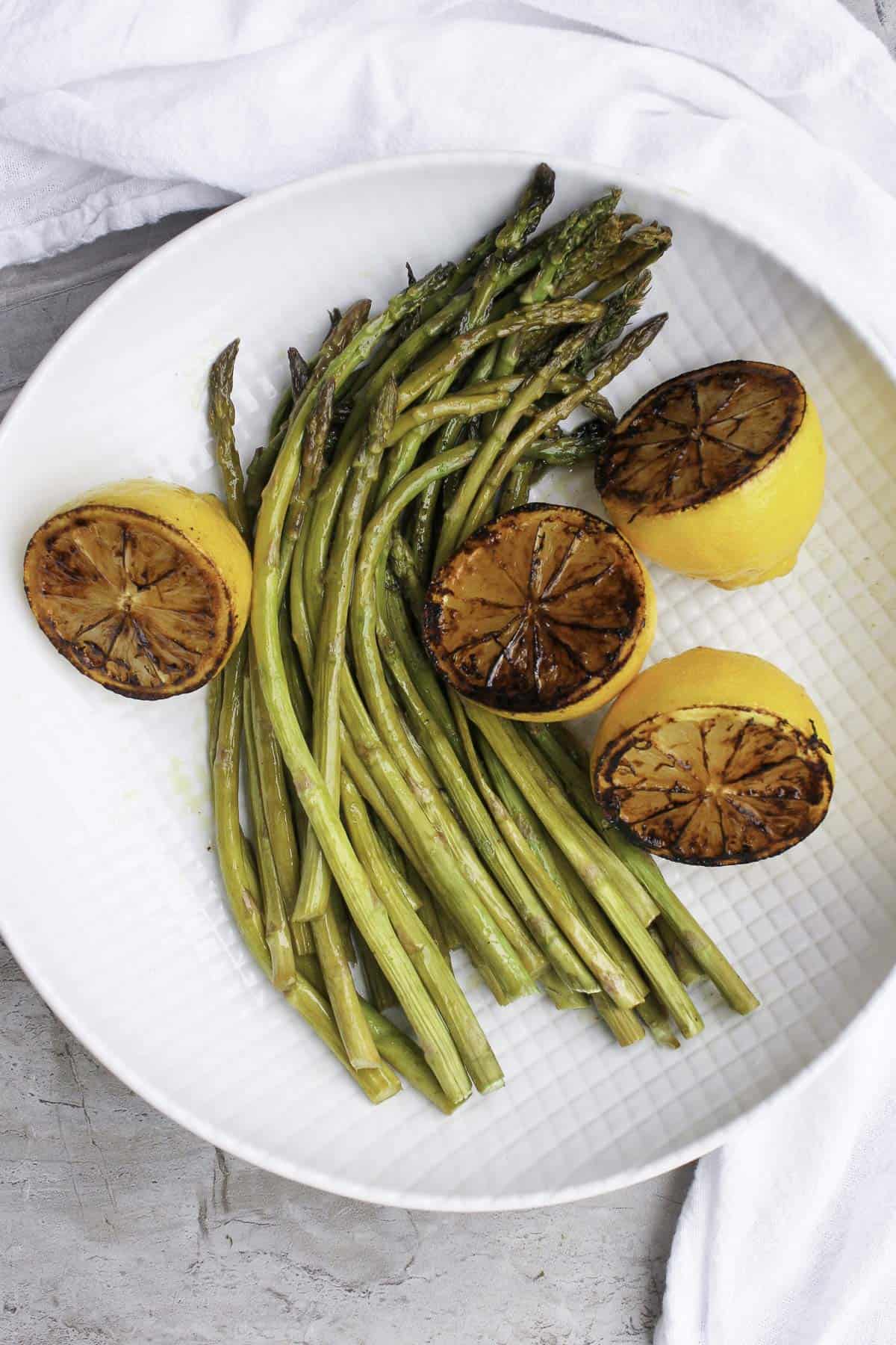 This Oven-Roasted Asparagus with Charred Lemon is drizzled with olive oil, white vinegar, and fresh lemon juice. It's fast, easy, and delicious! roasted asparagus with charred lemons on plate.