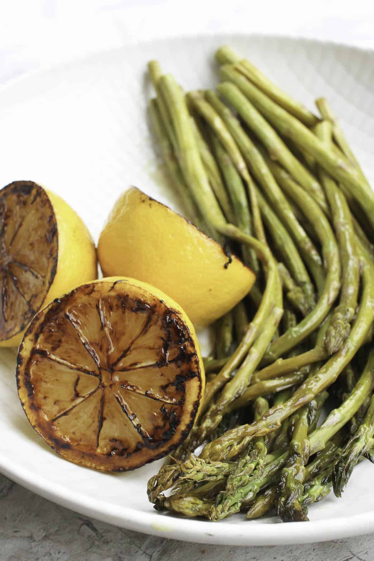 This Oven-Roasted Asparagus with Charred Lemon is drizzled with olive oil, white vinegar, and fresh lemon juice. It's fast, easy, and delicious! roasted asparagus with charred lemons on plate.