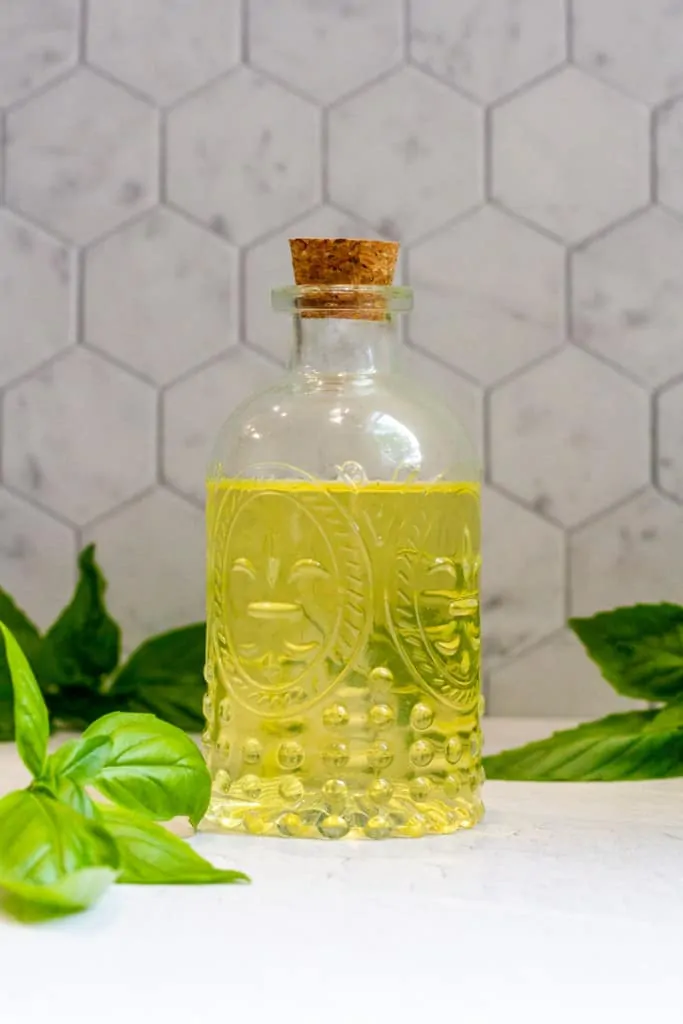 basil vinegar (basil flower vinegar) in a decorative jar on a Bessie Bakes White Textured Background + Hexagonal Tile Background.