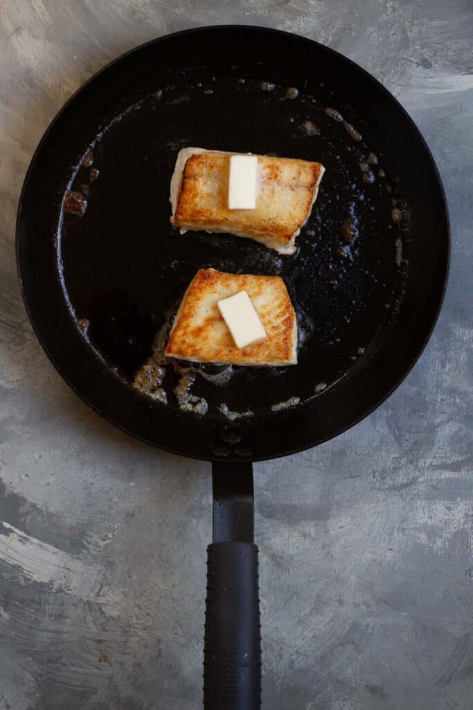 halibut filets in pan golden side up with butter on top.