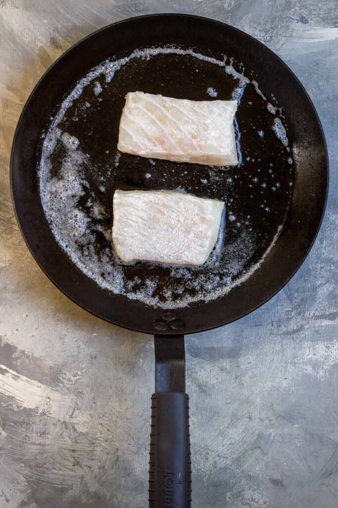 uncooked halibut fillets in a pan with butter.