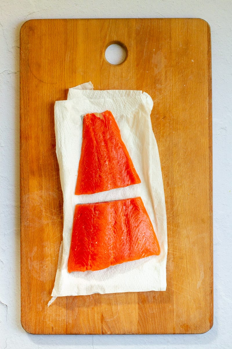 Salmon fillets on paper towel on wooden cutting board.