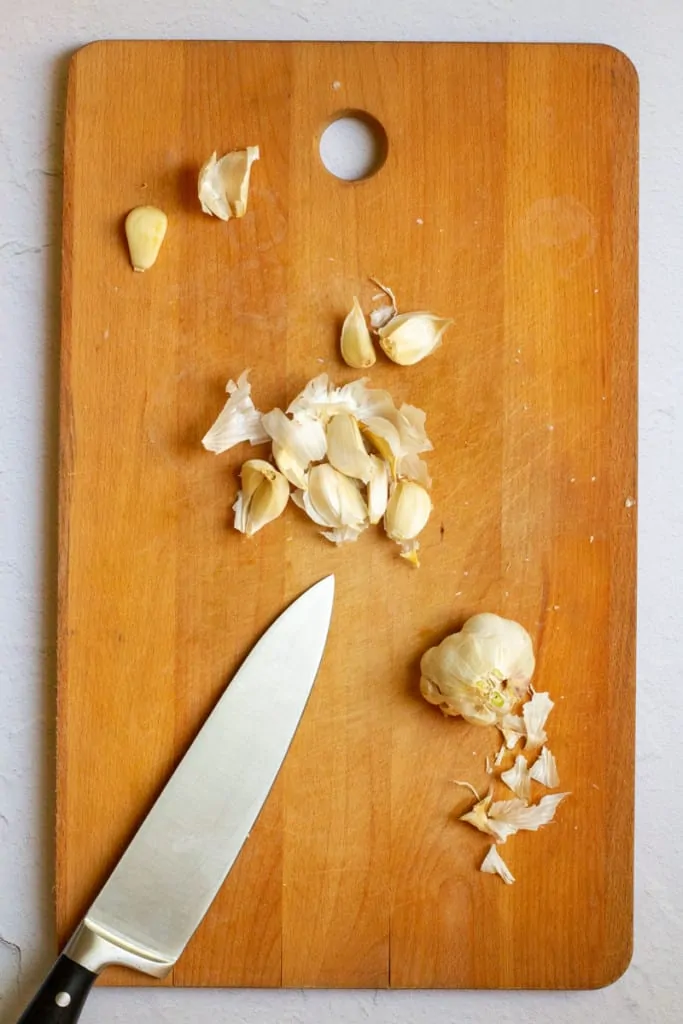 Knife on cutting board next to cloves.
