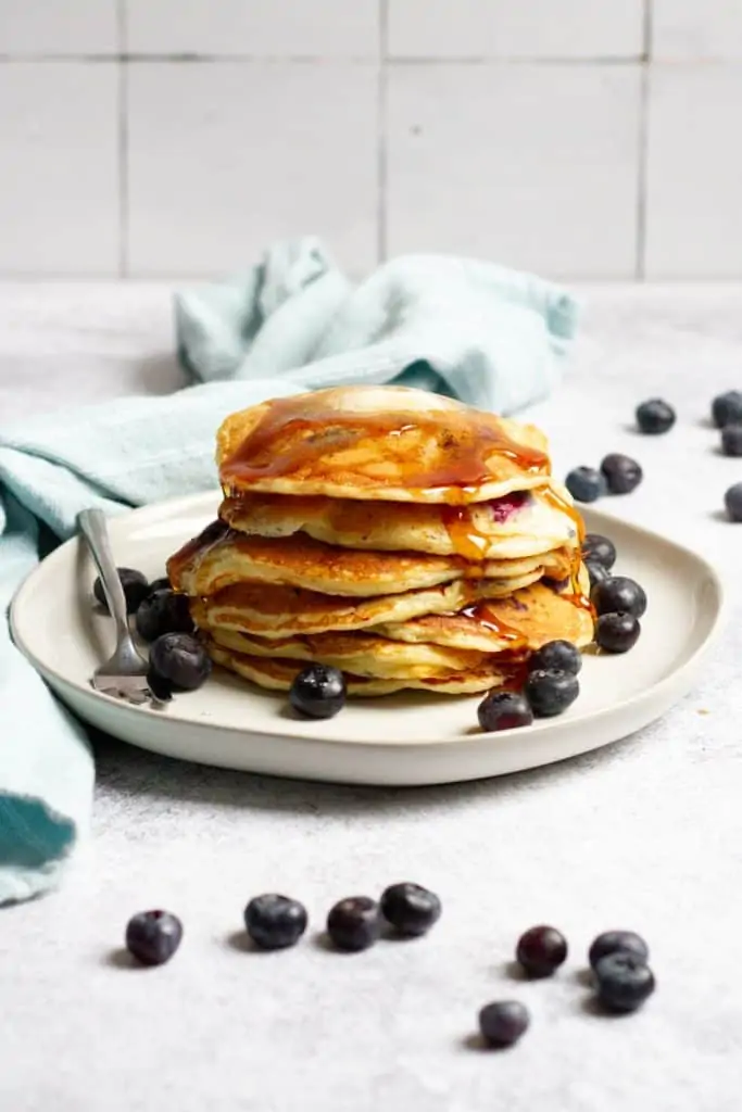 sourdough blueberry pancakes stacked on a plate with syrup and extra berries
