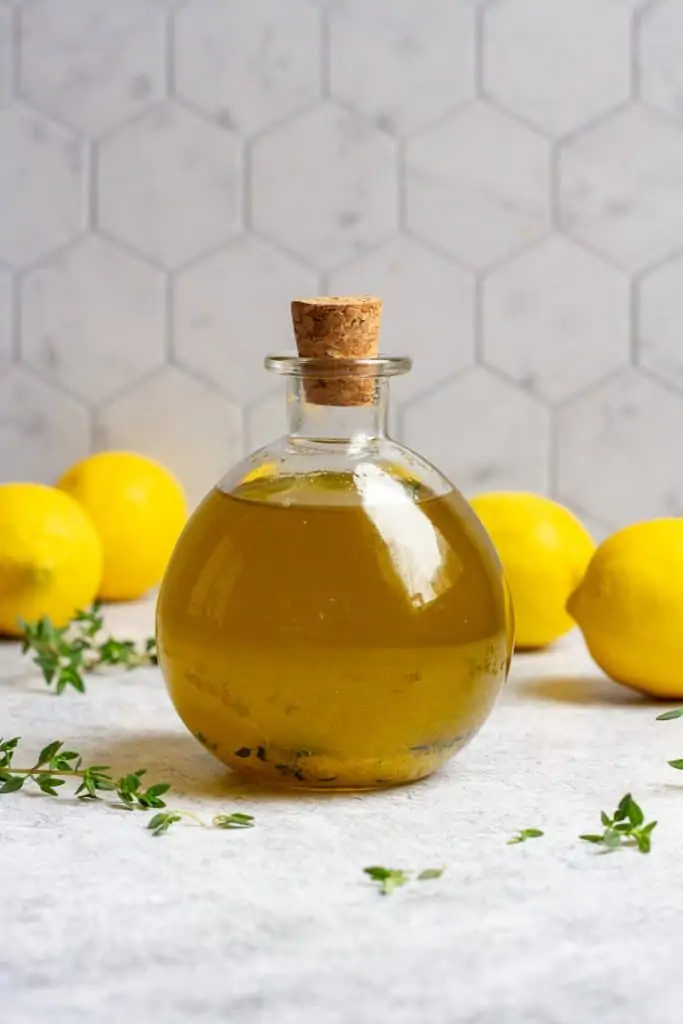 lemon olive oil in a glass bottle with lemons and herbs around the bottle