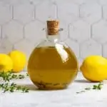 lemon olive oil in a glass bottle with lemons and herbs around the bottle