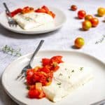Baked halibut with tomato caper sauce on plates.