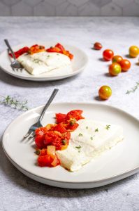 Baked halibut with tomato caper sauce on plates.