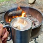 Campfire hot chocolate with peanut butter whiskey and toasted marshmallows in front of a campfire.