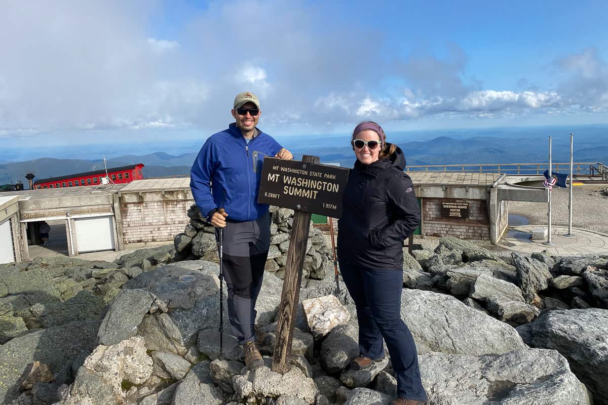 Man and woman standing at the sign for Mount Washington Summit.