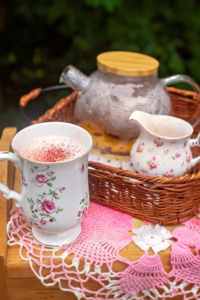 beet latte with rose in teacup next to wicker basket