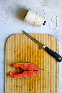 Salmon steak, boning knife + butcher's twine on cutting board.