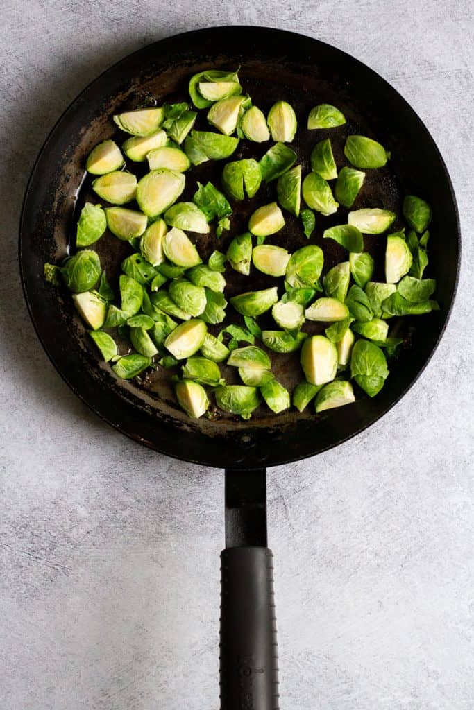 Uncooked brussels sprouts added to a large pan.