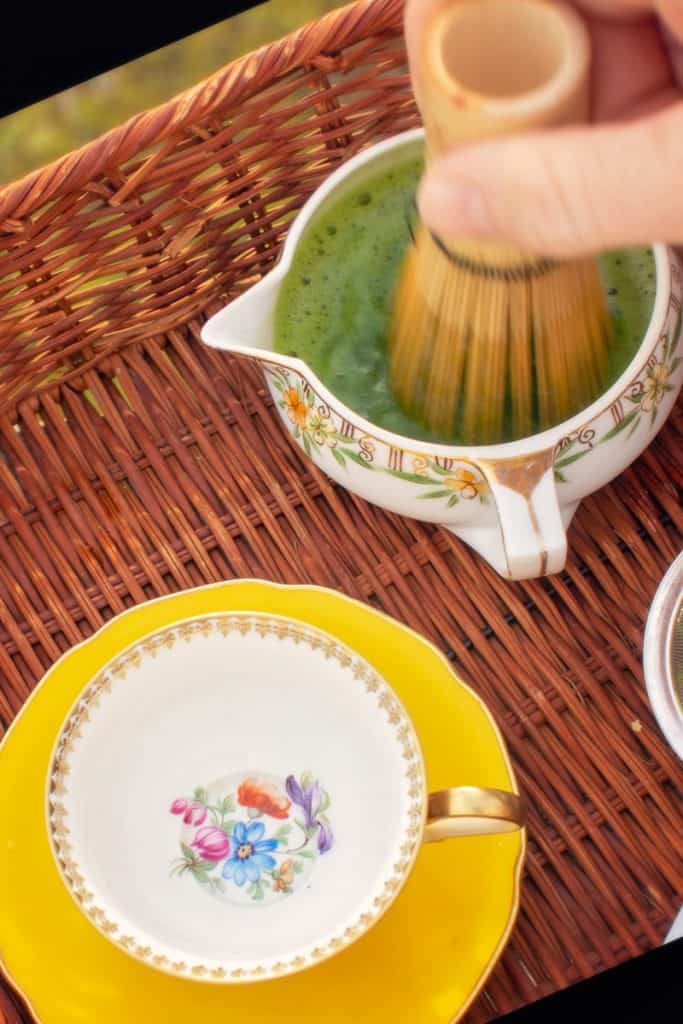 whisking matcha in small bowl next to teacup