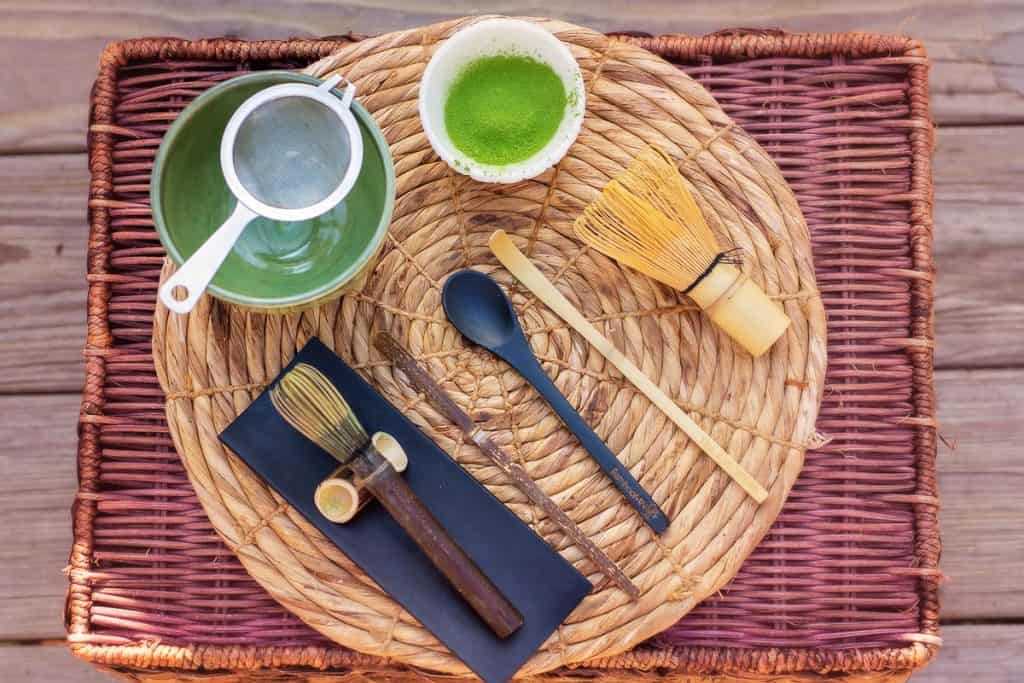 Matcha in cup, bamboo whisks, sieve, scoop and stirrer needed to make vanilla matcha latte