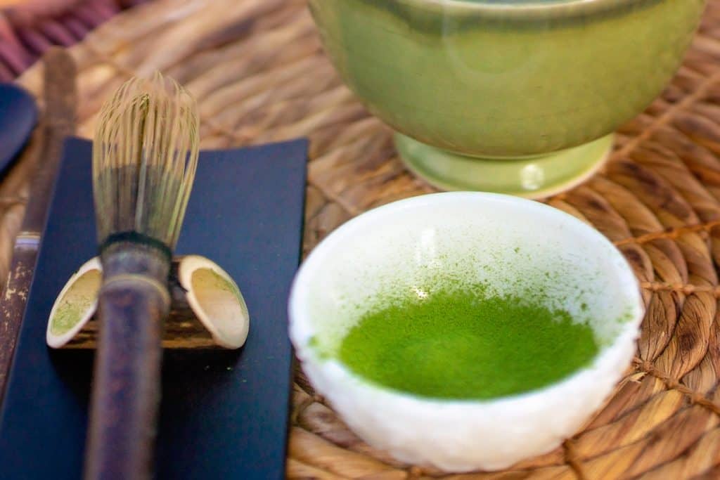 Matcha tea in small bowl with bamboo whisk